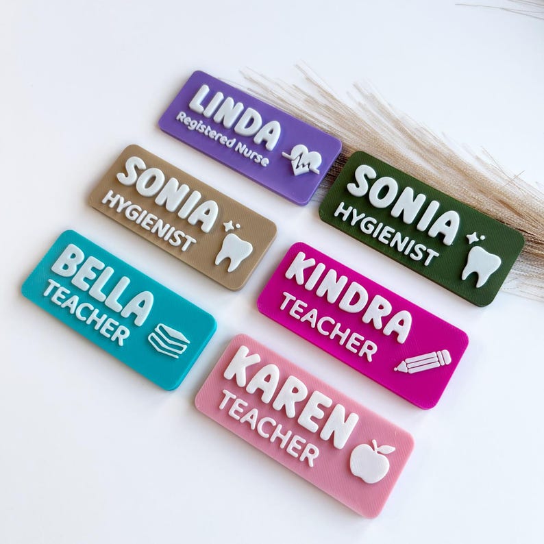 May include: Six rectangular name badges in purple, tan, olive green, teal, magenta, and pink. Each badge features raised white lettering and icons including a heart, tooth, book stack, pencil, and apple, displaying names and professional titles.