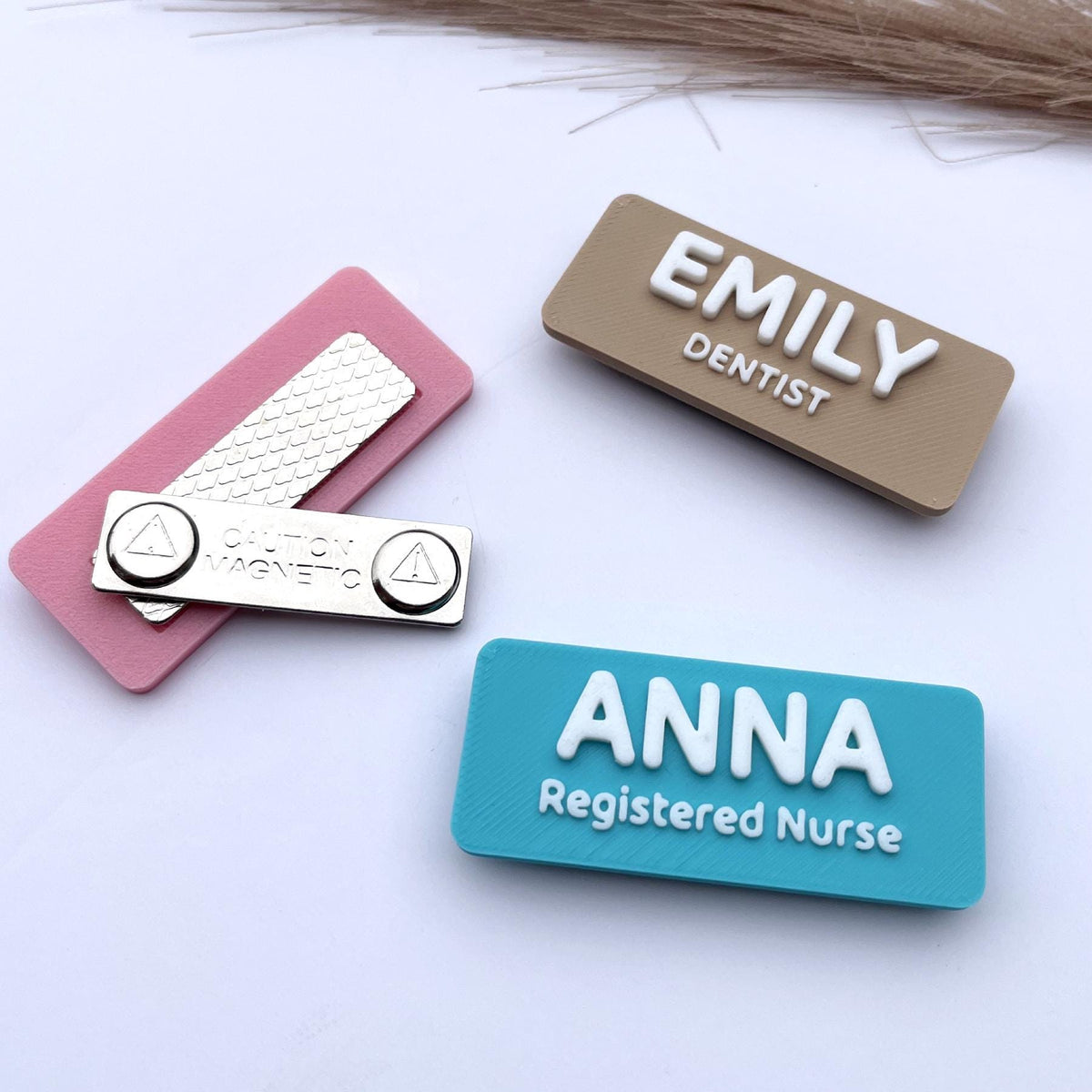 May include: Three name badges with magnetic backings. One is pink with a silver magnetic bar and a silver badge that reads "CAUTION MAGNETIC". The other two are rectangular, one tan with "EMILY DENTIST" and the other blue with "ANNA Registered Nurse".