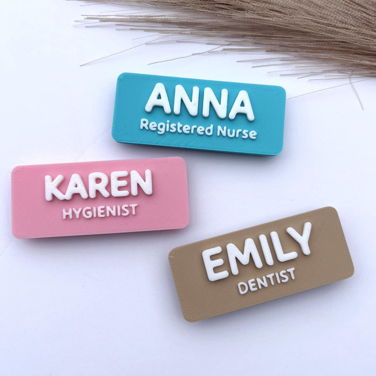 May include: Three rectangular name badges in teal, pink, and tan. Each badge has a white 3D-printed name and title: "ANNA Registered Nurse", "KAREN Hygienist", and "EMILY Dentist".
