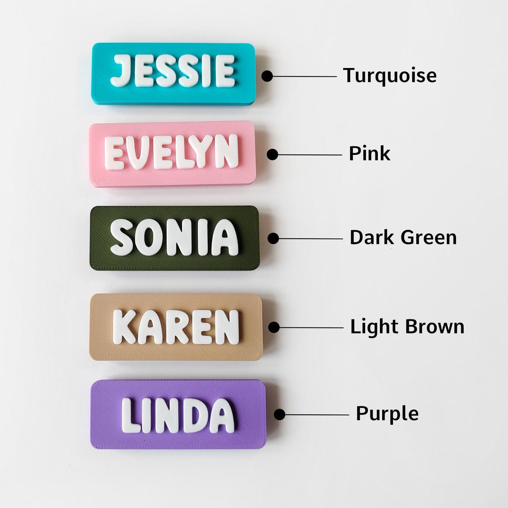 May include: A selection of rectangular name tags in turquoise, pink, dark green, light brown, and purple. Each tag displays a name in white, block letters: JESSIE, EVELYN, SONIA, KAREN, and LINDA. The tags have a 3D appearance.