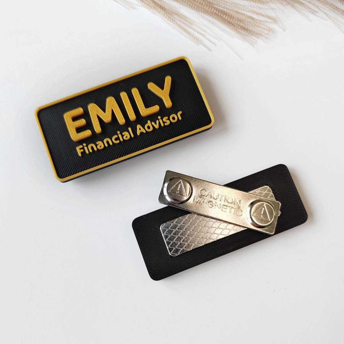 May include: A black and gold name tag displaying the name "EMILY" and the title "Financial Advisor". Includes a magnetic backing with the text "CAUTION MAGNETIC".